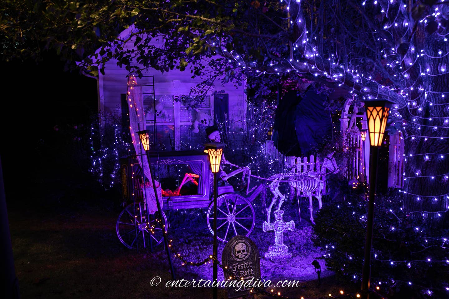 Halloween graveyard lit with purple string lights, purple flood lights and orange lanterns