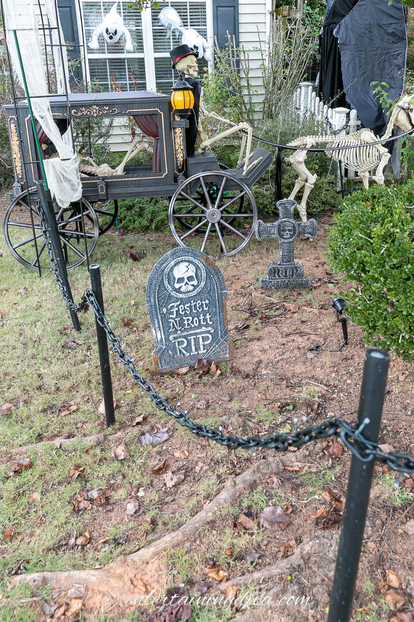 Chain fence surrounding a Halloween graveyard with tombstones and a skeleton horse and carriage