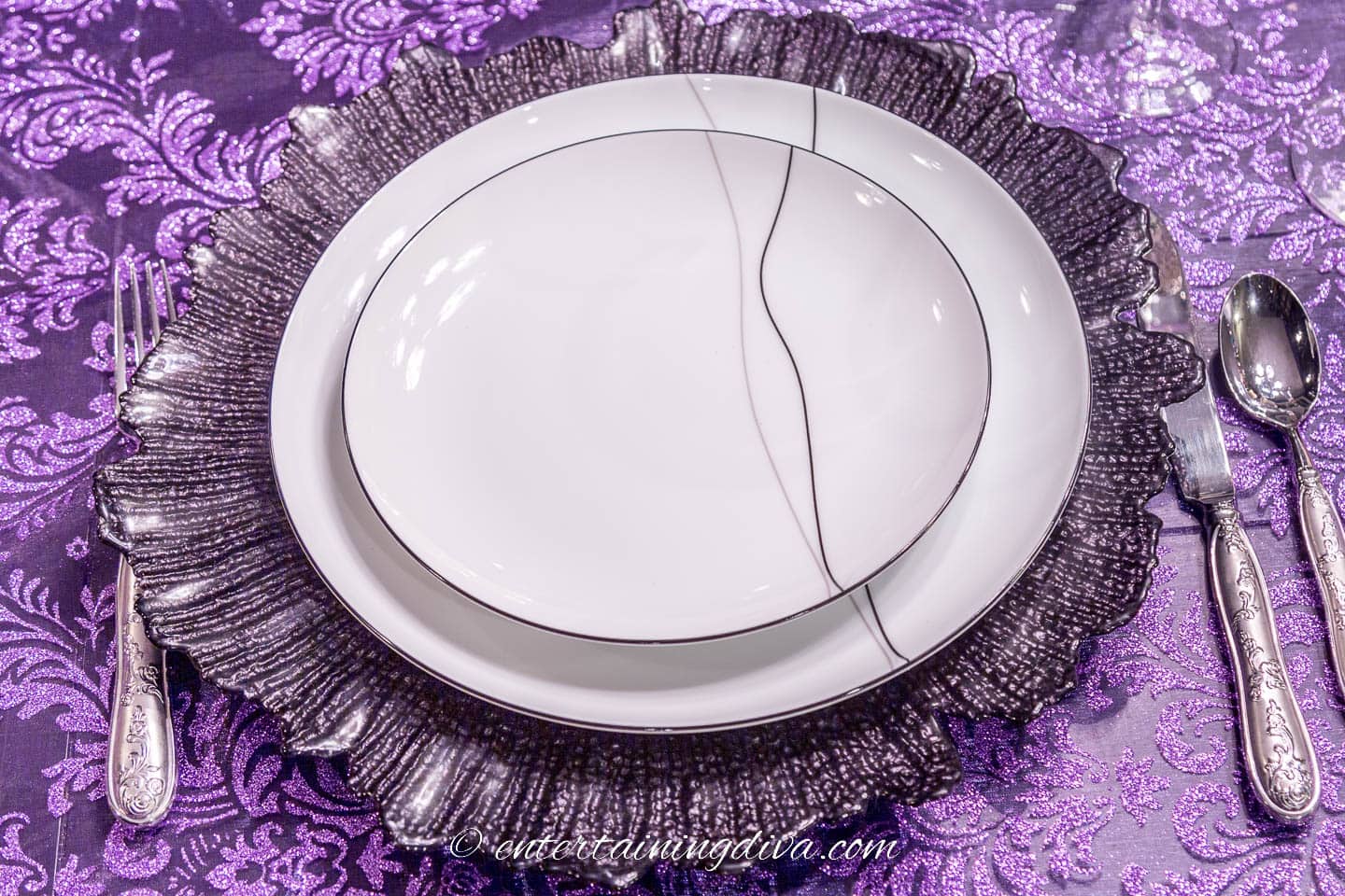 Place setting with black and white plates on a black charger and purple tablecloth