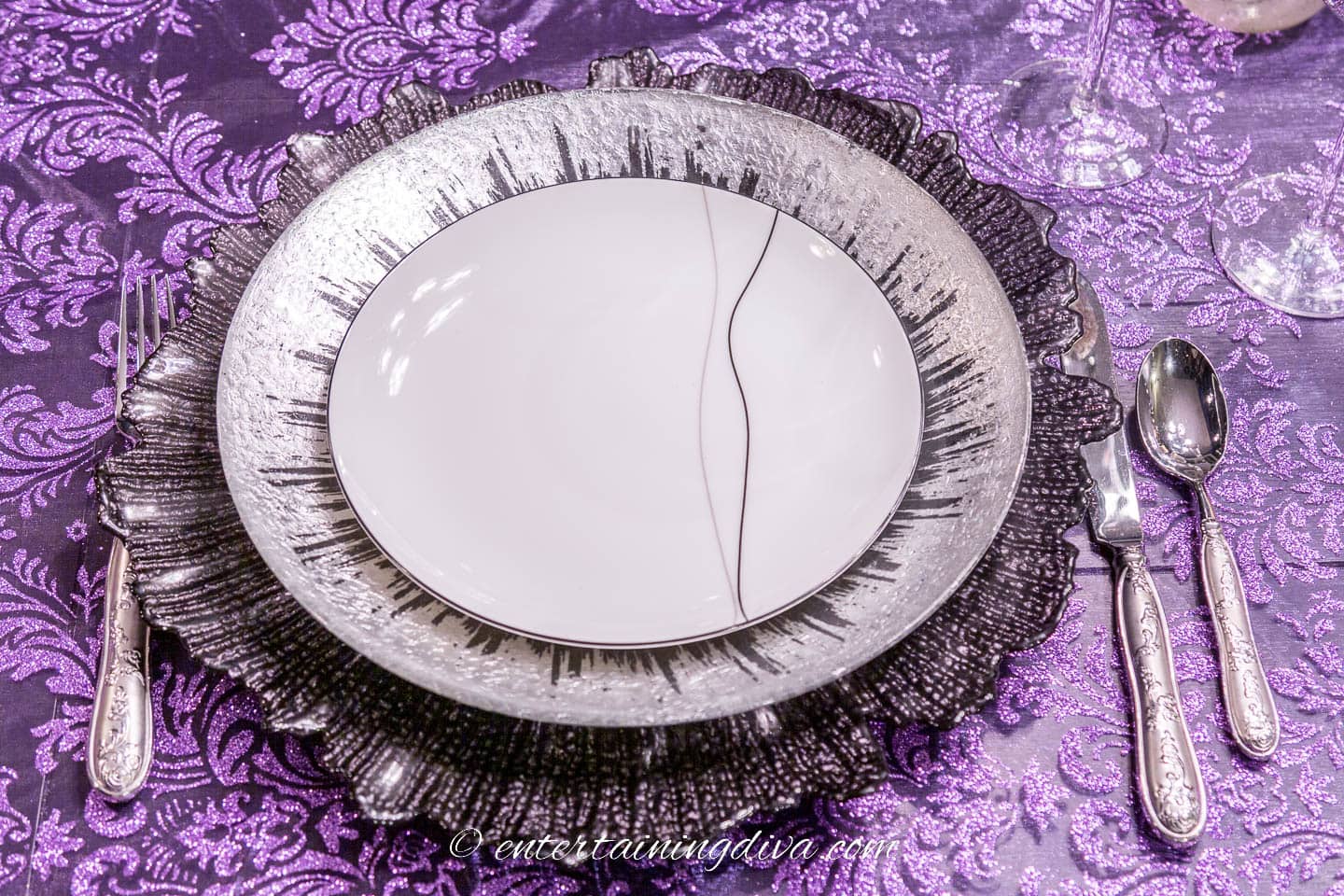 Place setting with black and white salad plate on a silver dinner plate with a black charger and purple tablecloth