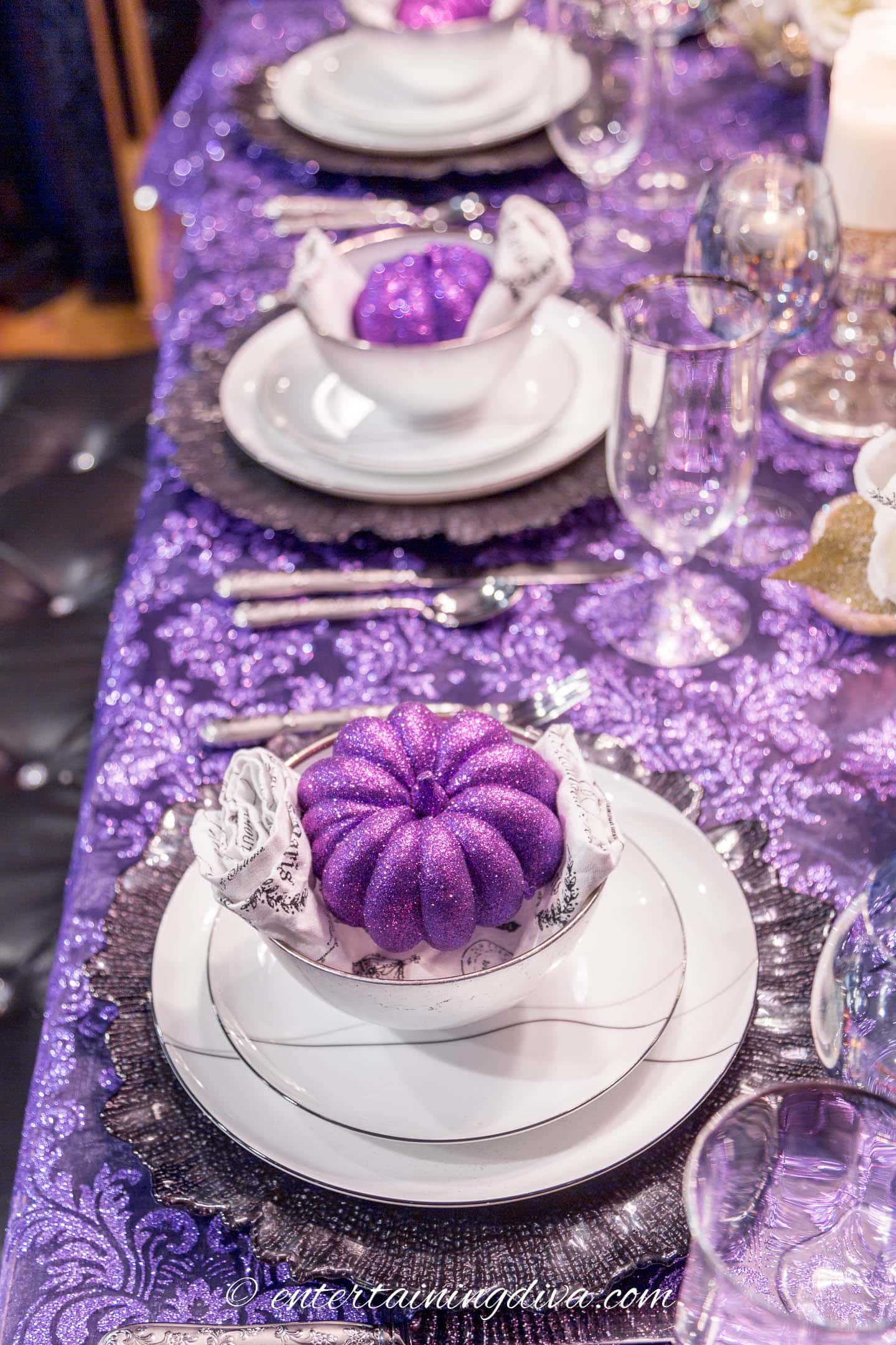 Three black and white place settings with purple pumpkins on a purple lace tablecloth
