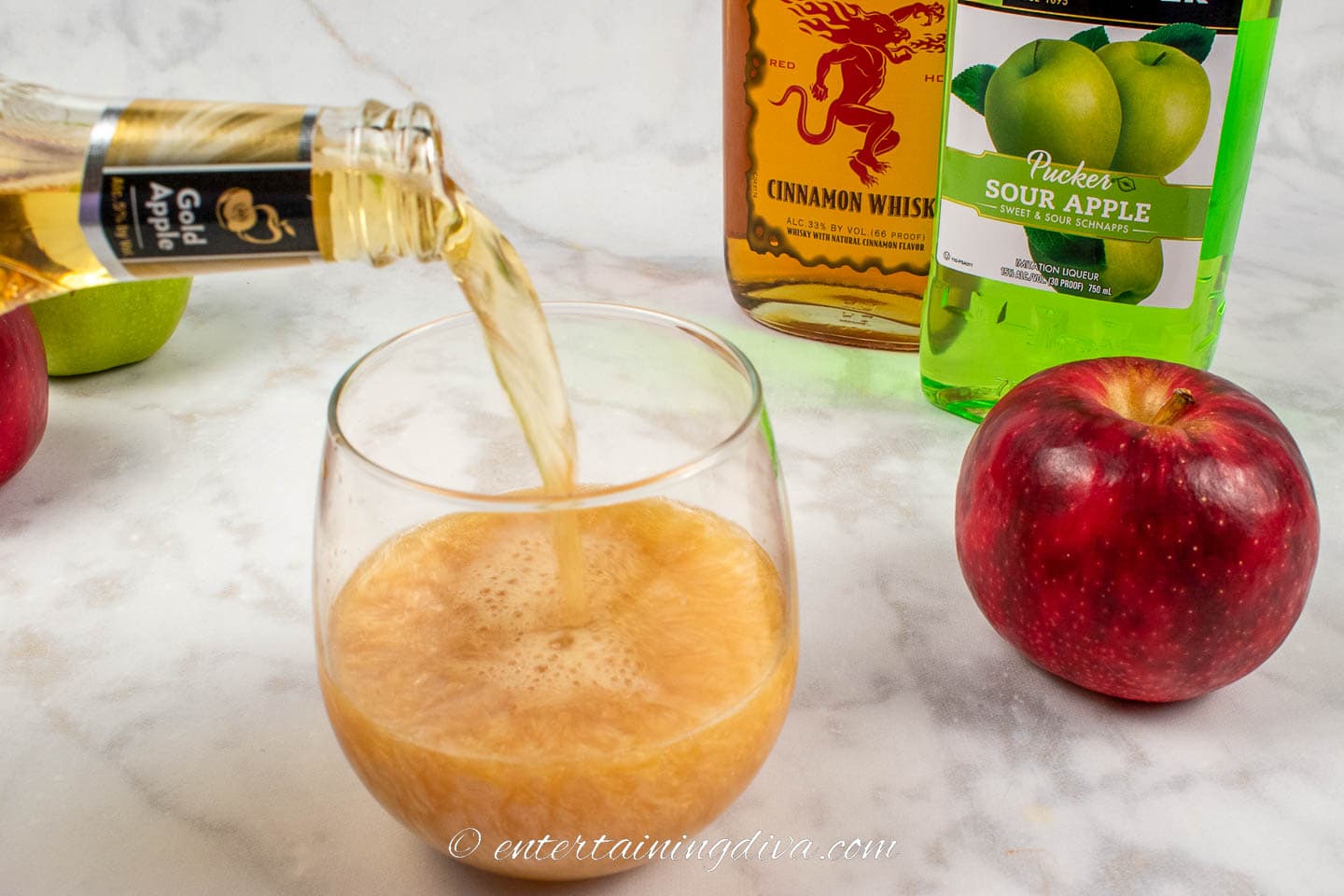 hard cider being poured into a glass with bottes of fireball and apple pucker in the background
