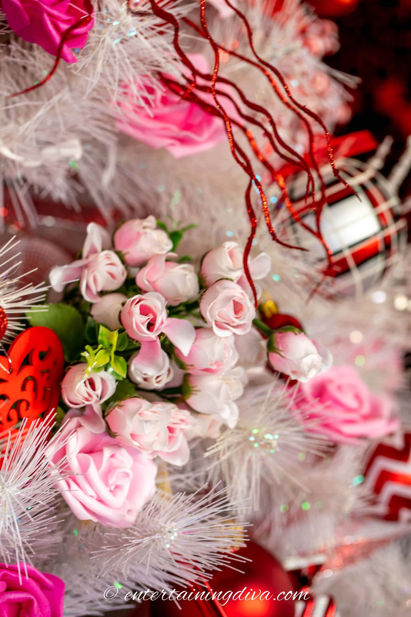 A bunch of small pink faux roses with red ornaments on a white Valentine tree