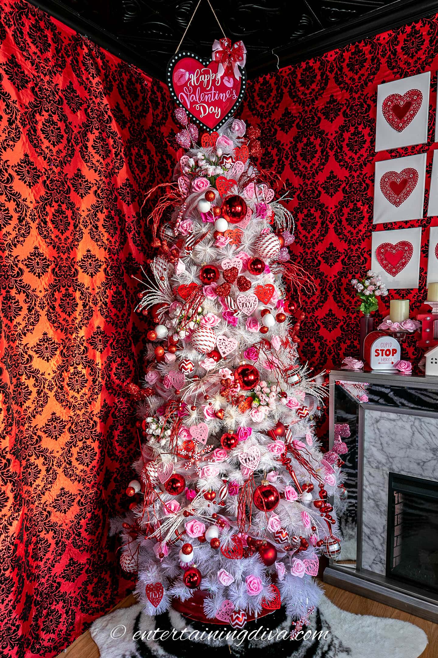 White Valentine tree with pink and red ornaments and a heart tree topper in front of walls covered in red and black fabric