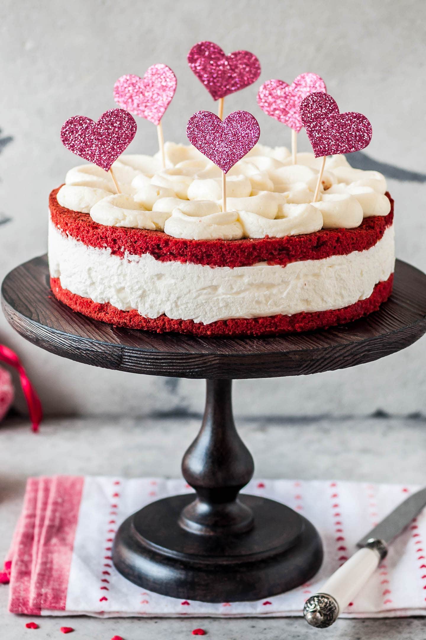 Naked red velvet cake on a tray with heart toppers stuck in the top of it
