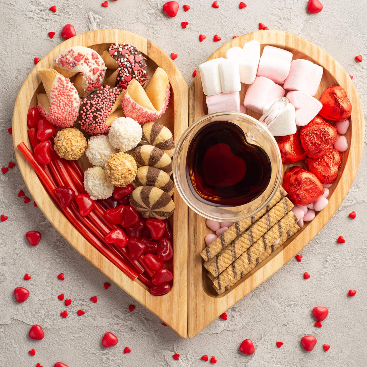 Heart-shaped Valentine charcuterie board with various pink and red candies as well as cookies
