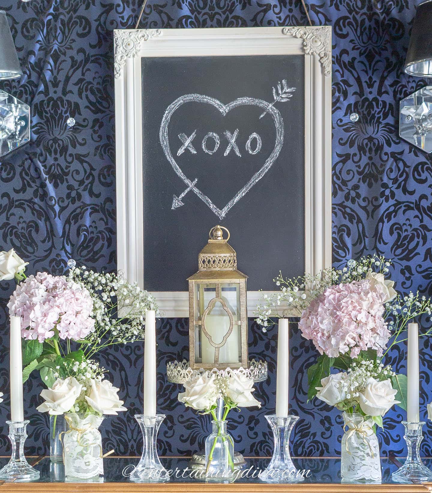 Candle lantern with bouquets of pink hydrangeas and white roses in front of a chalk board sign with a heart on it as part of Valentine tea party decorations on a buffet