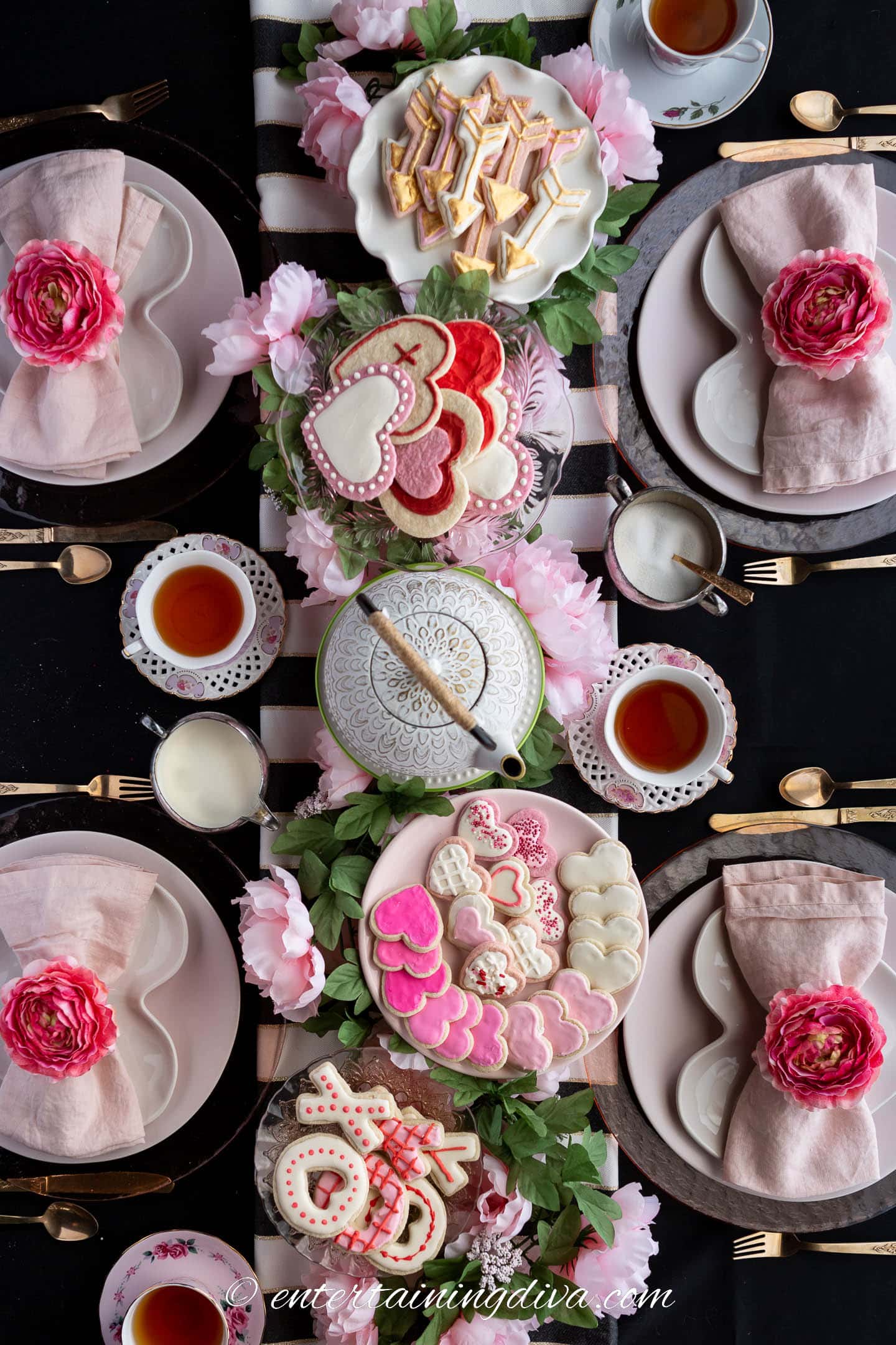 Valentine Day tea party centerpiece made with faux flowers, heart and arrow sugar cookies on cake stands and a tea pot on a cake stand