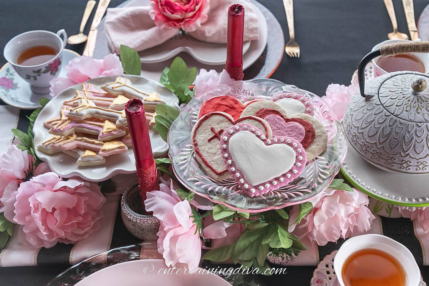 A Valentine tea party centerpiece with heart sugar cookies, candles, faux flowers and a tea pot