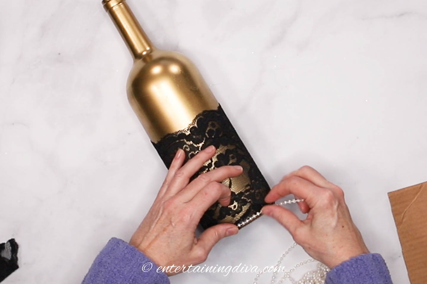 A string of faux pearls being attached to the bottom of the wine bottle