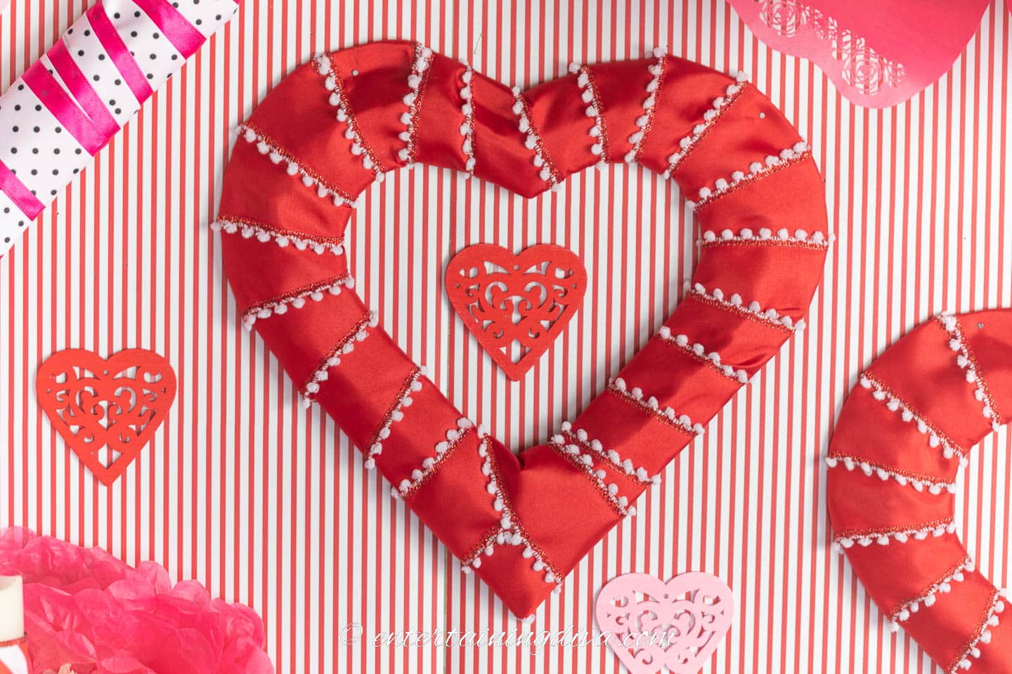 DIY red heart wreath hung on a wall with red and whit stripes in the background