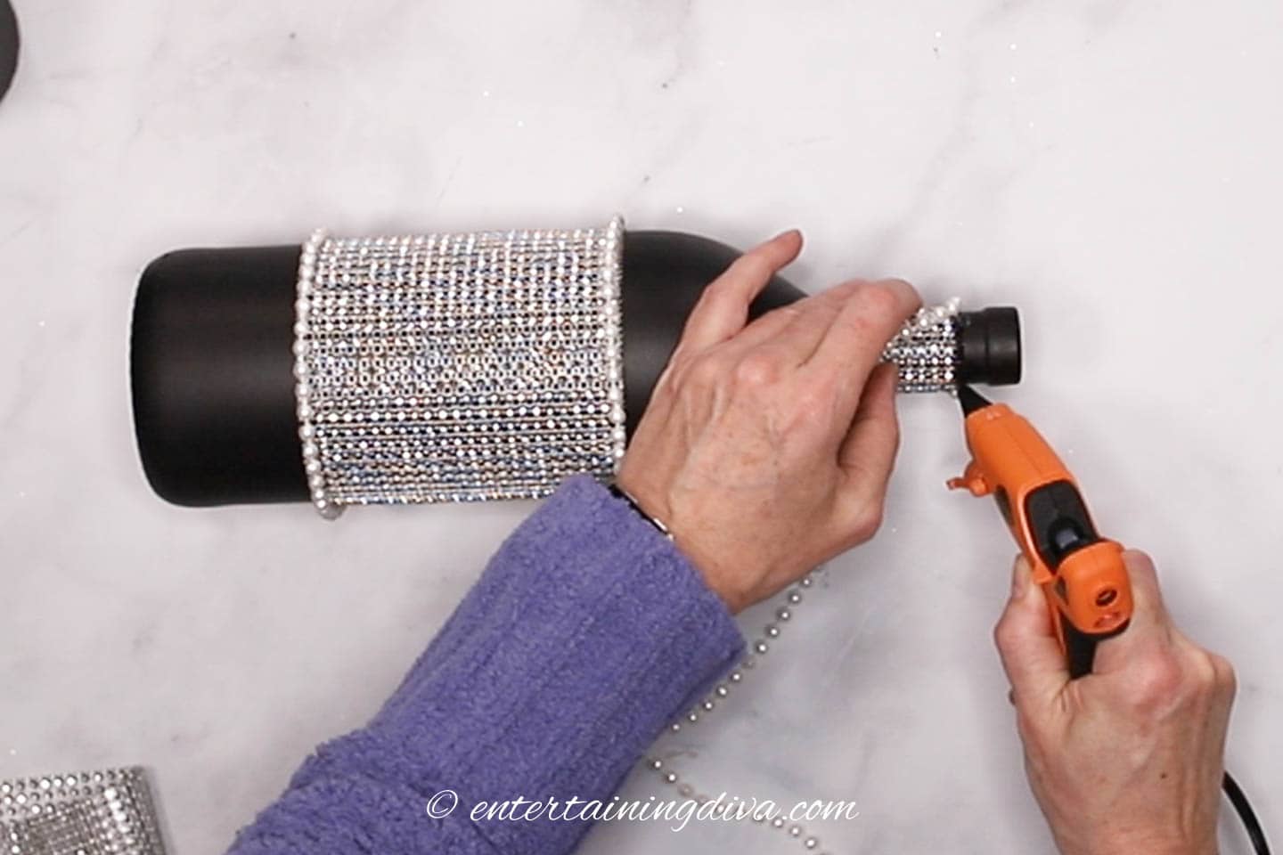 Faux pearls being glued to the top edge of silver ribbon around the neck of a wine bottle