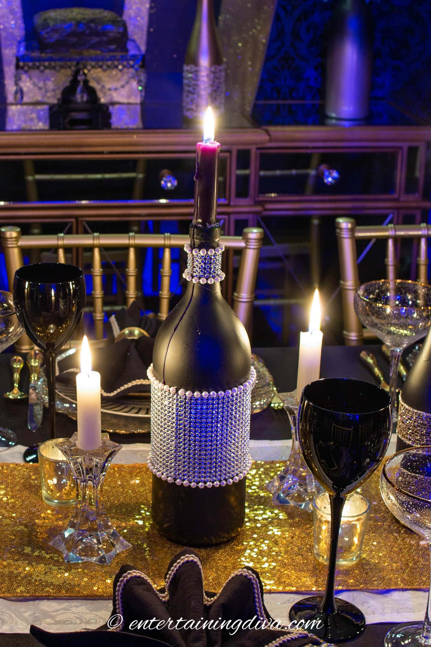 DIY rhinestone black wine bottle with pearls used as a candleholder in a centerpiece for a black and gold table setting