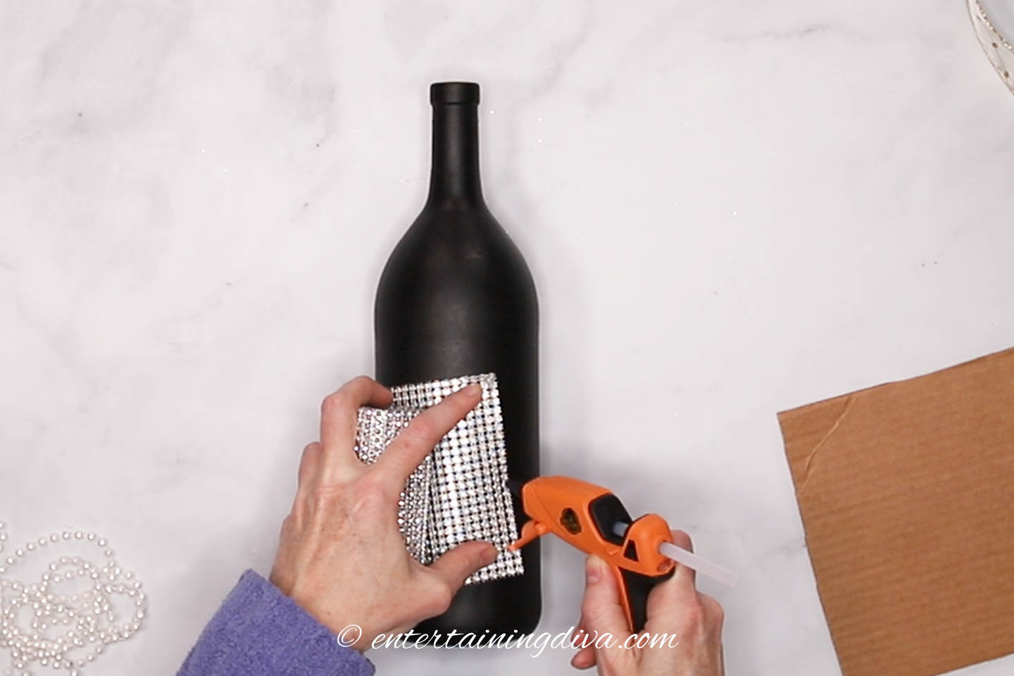 wine bottle with glue gun putting glue on rhinestone ribbon