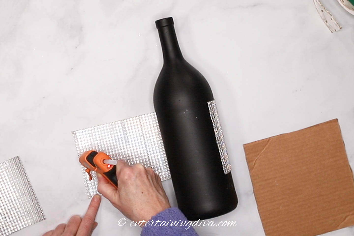 glue gun putting glue on rhinestone ribbon to be wrapped around a wine bottle