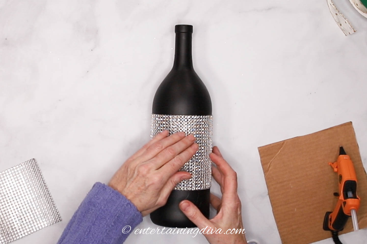 rhinestone ribbon being glued on to the middle of a black wine bottle