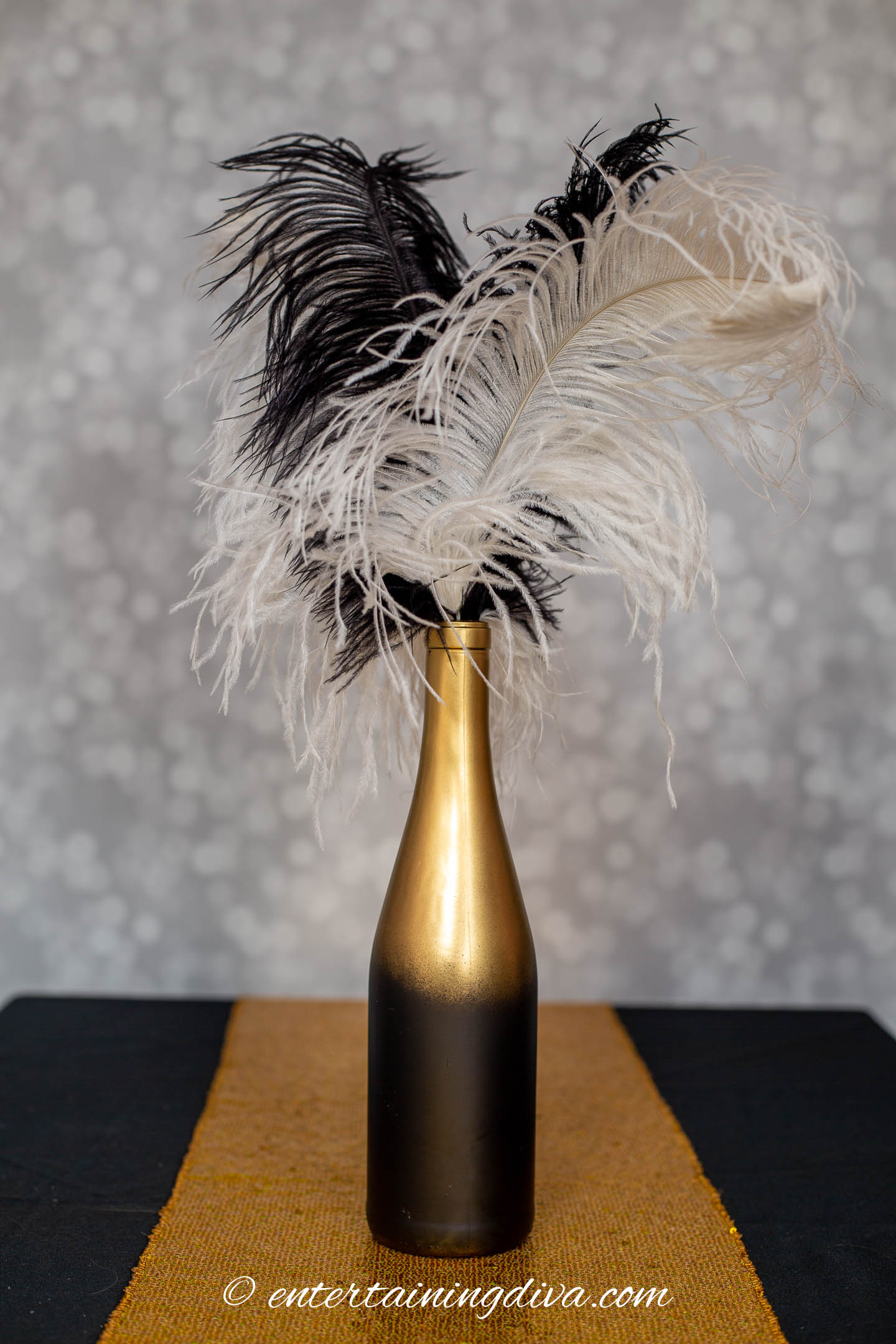 Wine bottle spray painted black and gold with white and black ostrich feathers in it