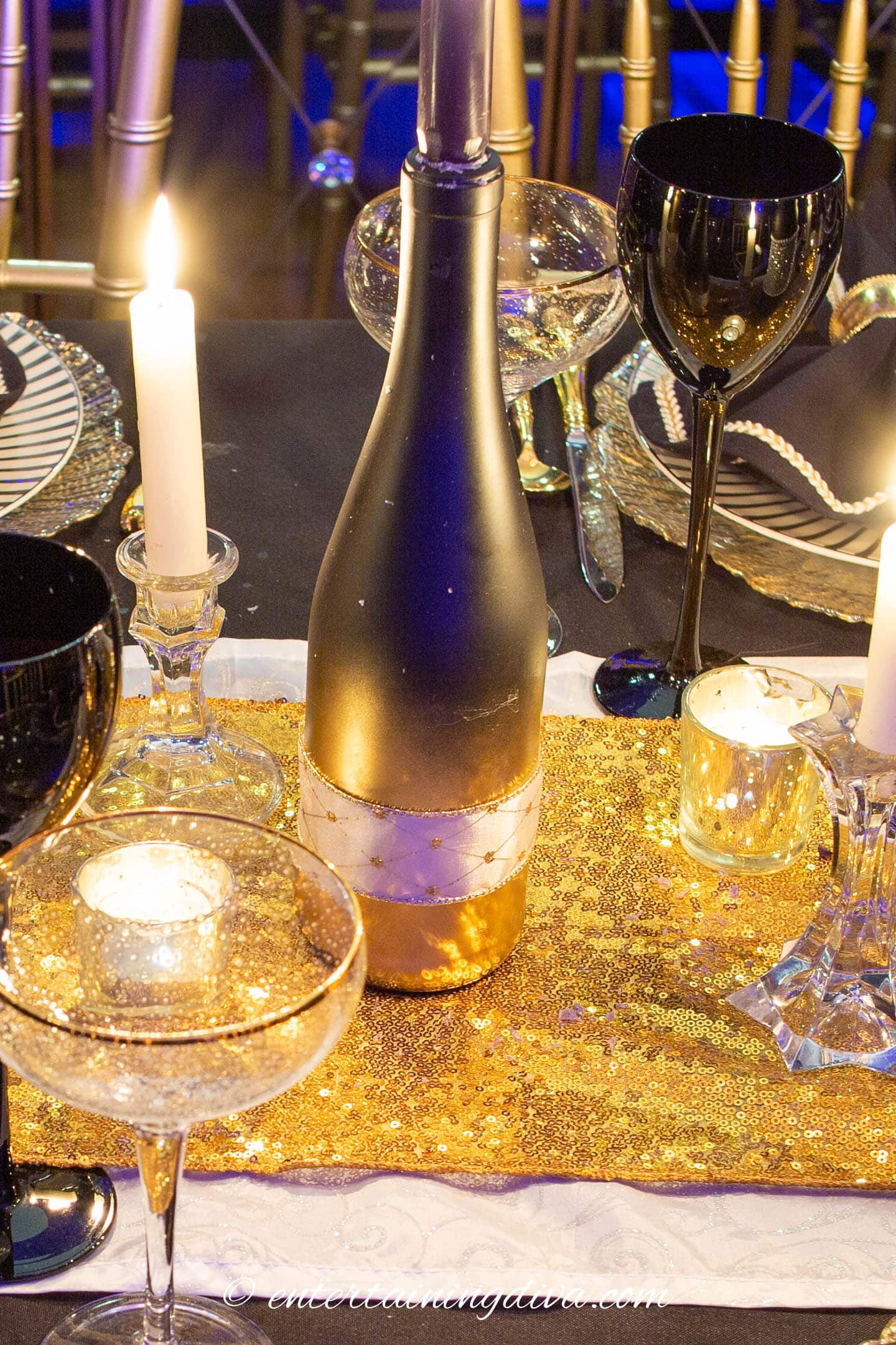 A black and gold wine bottle used as a candleholder in a black and gold table centerpiece