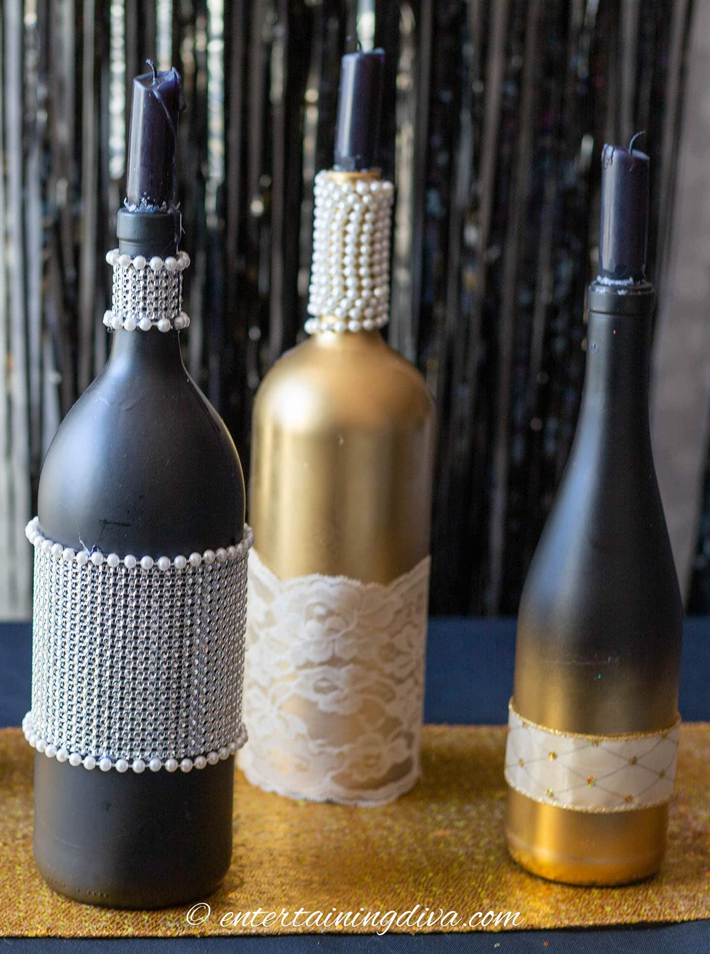 Gold and black spray painted wine bottles that have been decorated with lace, ribbon, rhinestones and pearls