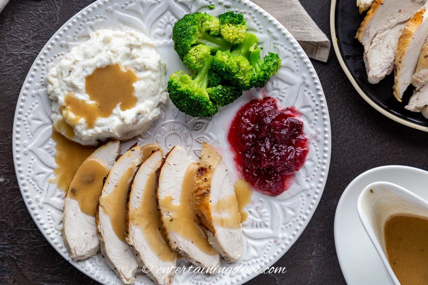 Plate with broccoli, cranberry sauce, mashed potatoes and turkey covered with turkey gravy