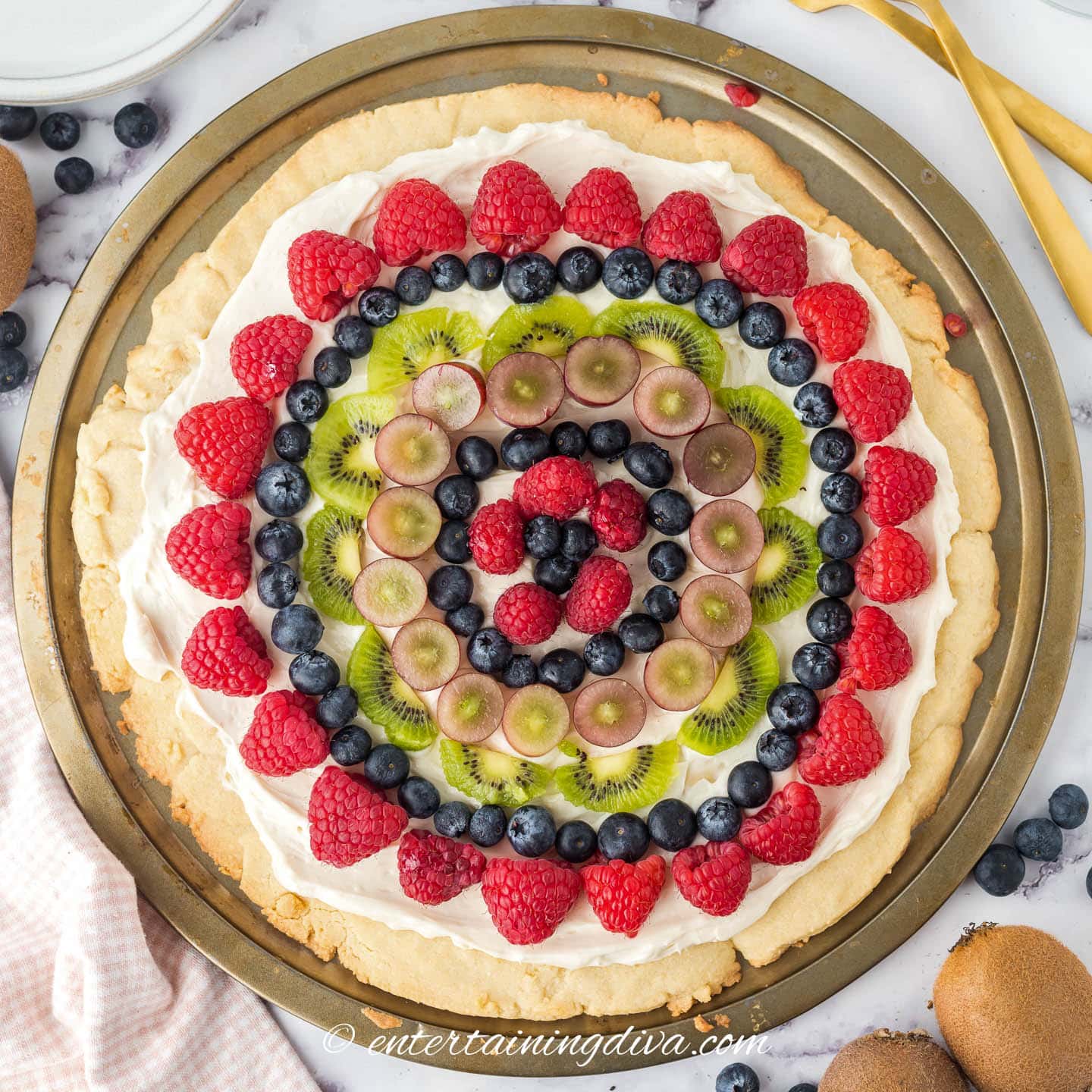 Fruit pizza with a sugar cookie crust, cream cheese frosting and blueberries, raspberries, grapes and kiwi toppings