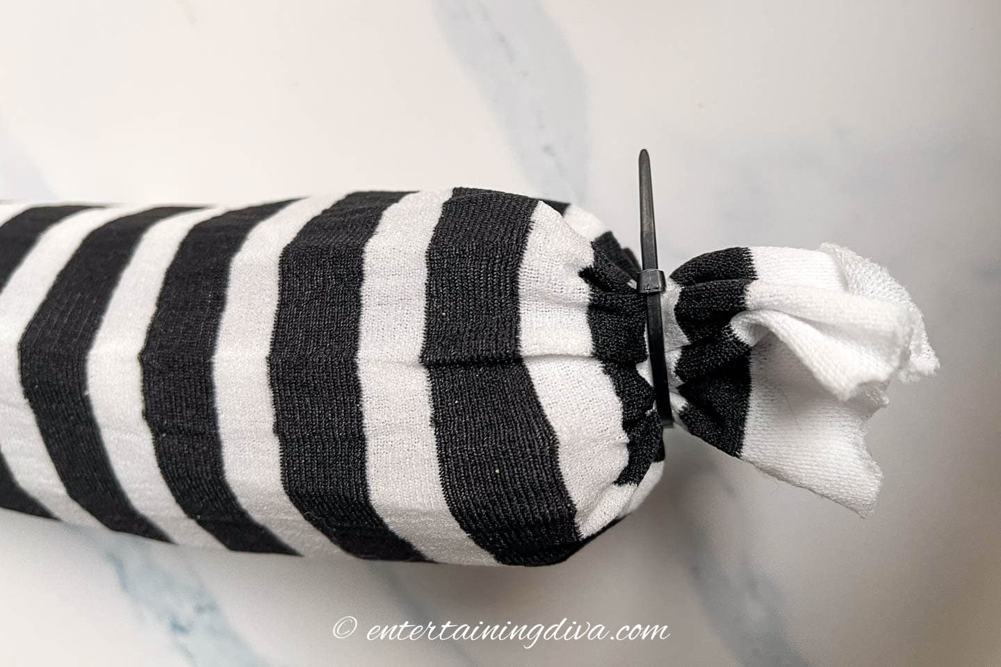 Zip tie around the end of a "sandworm" made from a black and white striped stocking and a pool noodle