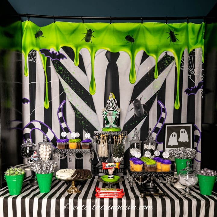 A Halloween dessert table with green and black decorations and a Beetlejuice backdrop behind it.