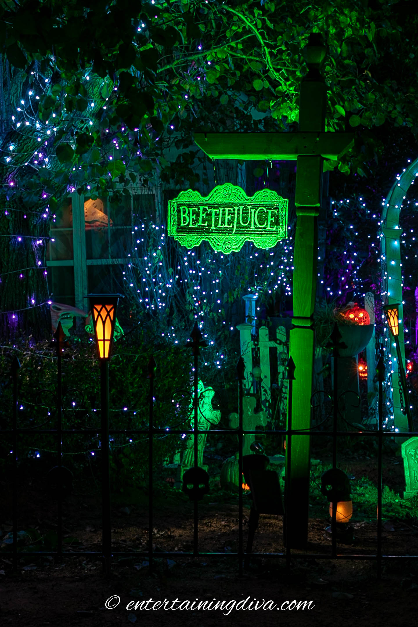 A yard decorated for Halloween with green lights and a Beetlejuice sign.