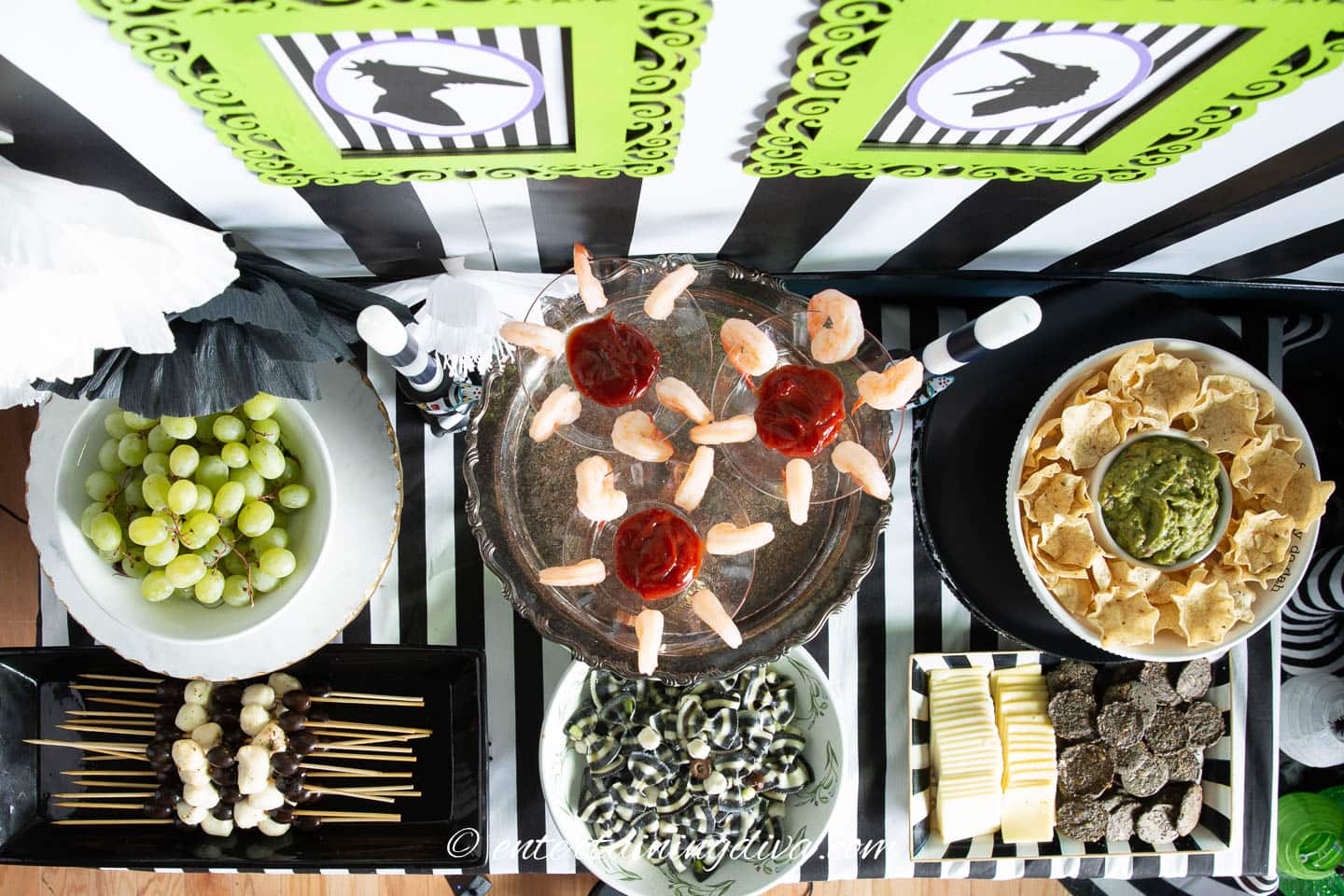 A black and white striped table with a variety of food on it for a Beetlejuice themed party