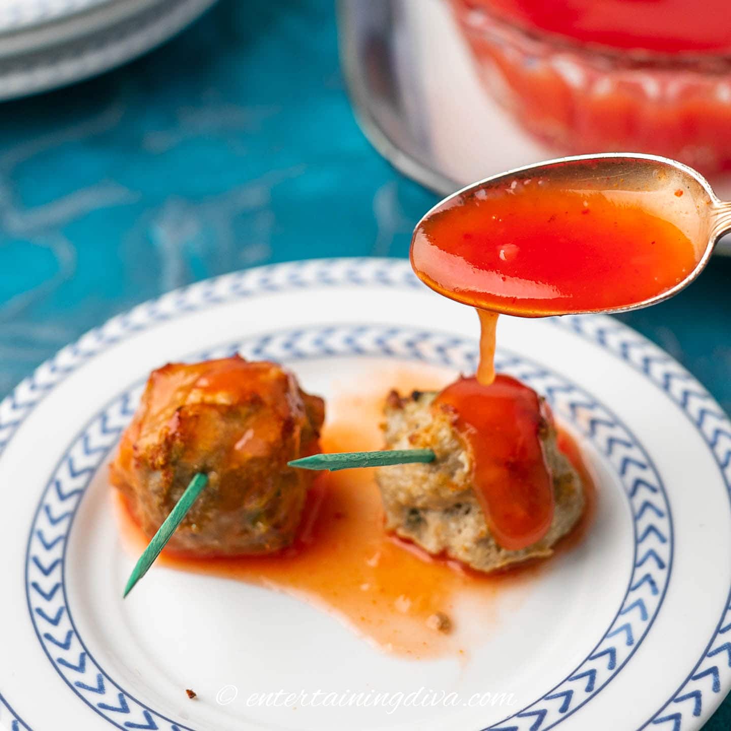 A spoon is being used to pour red sauce over meatballs.