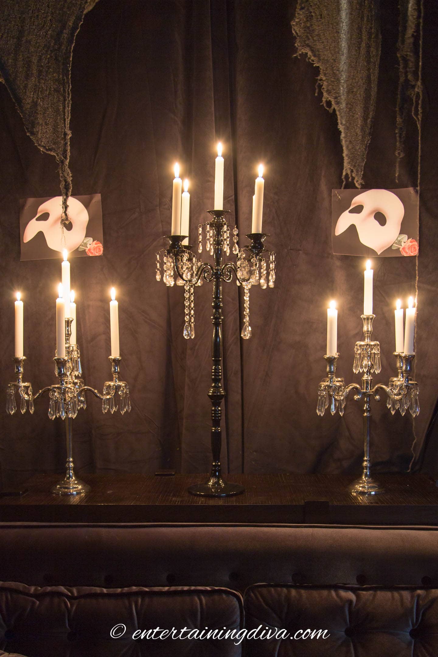 Candelabras in front of black velvet curtains with pictures of Phantom of the Opera masks on them
