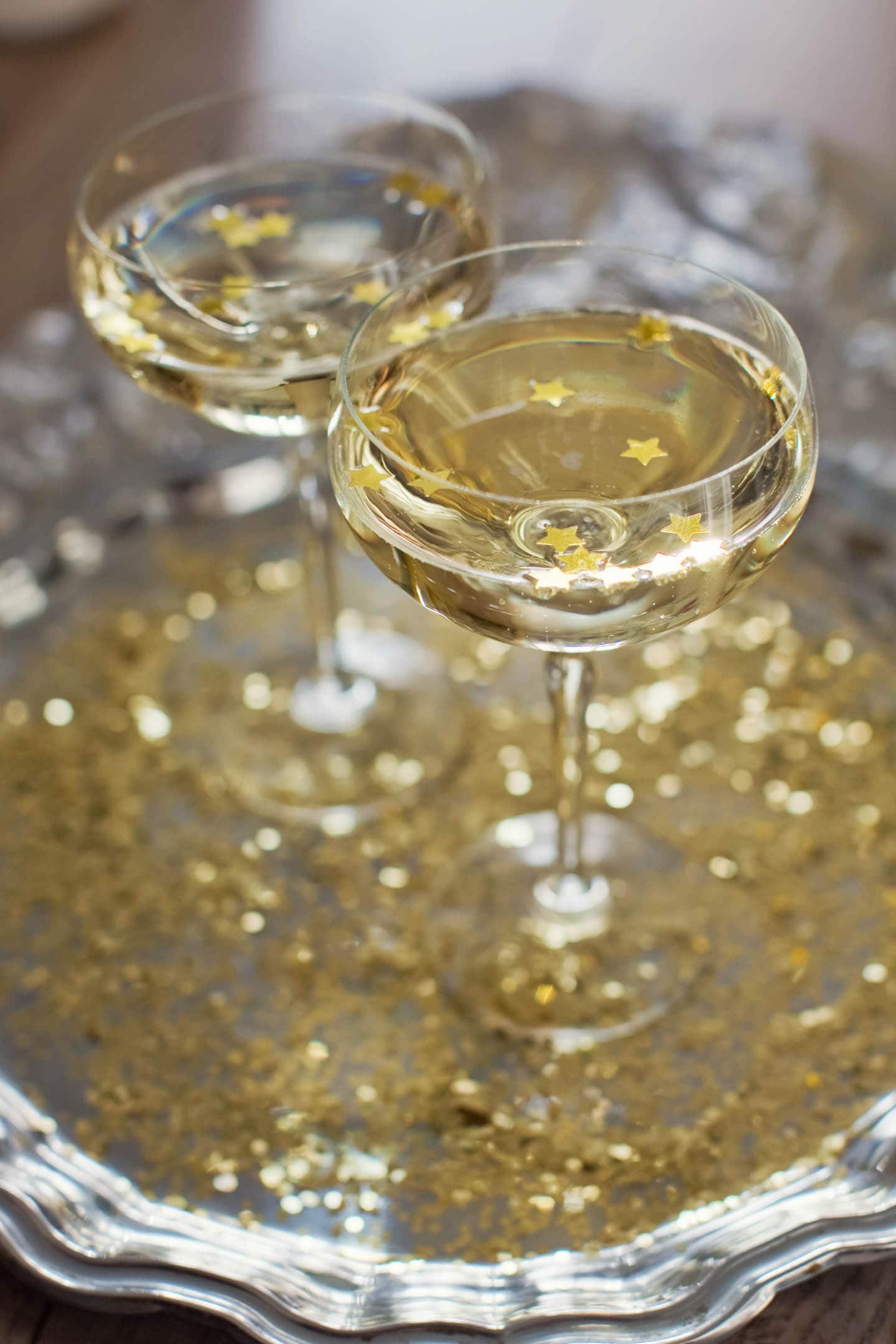 Two champagne glasses on a silver tray with gold confetti.