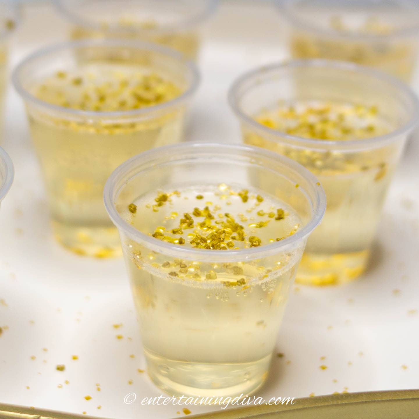 A tray of gold champagne jello shots with gold sprinkles on them.
