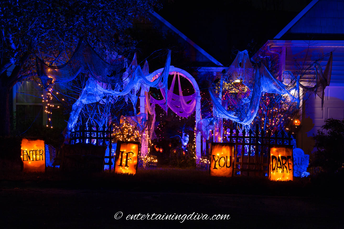 A front yard decorated with blue and orange Halloween outdoor lighting and "Enter If You Dare" luminaries