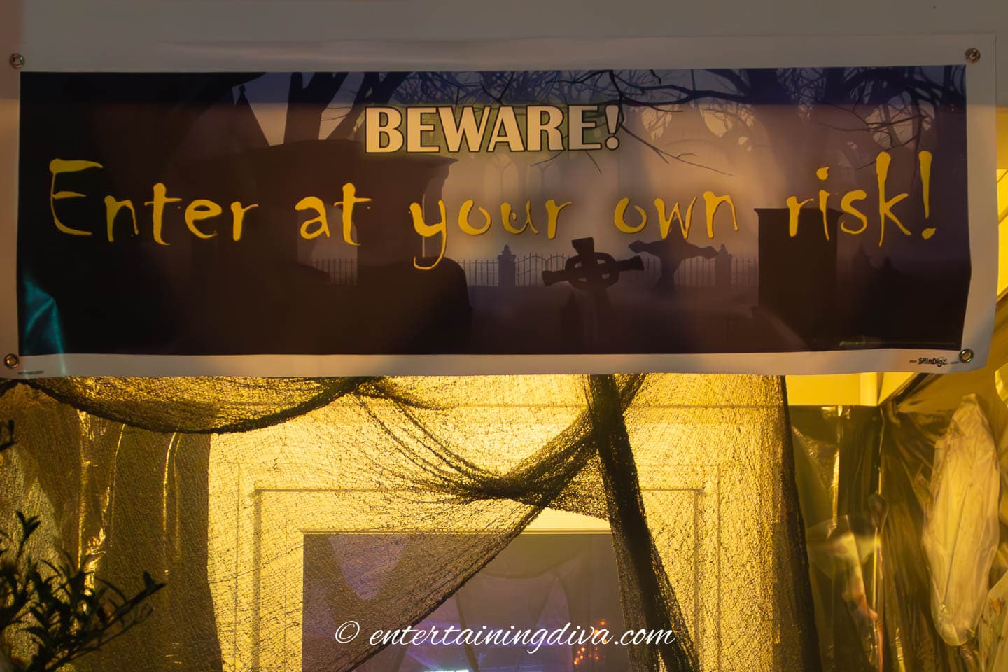 Yellow Halloween outdoor lighting behind a sign that says beware enter at your own risk.