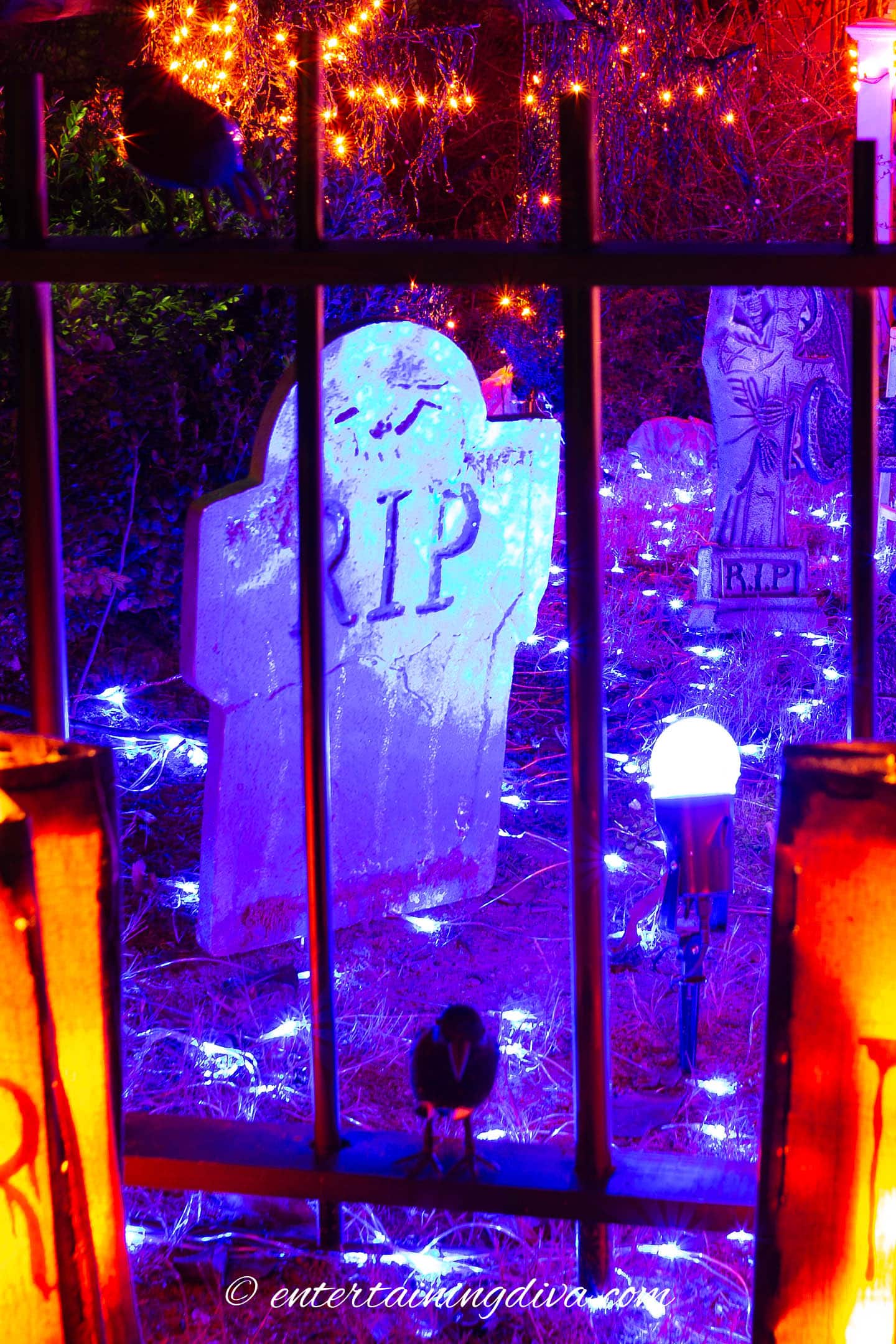 A spooky metal fence with a view of a graveyard, illuminated by Halloween outdoor lighting.