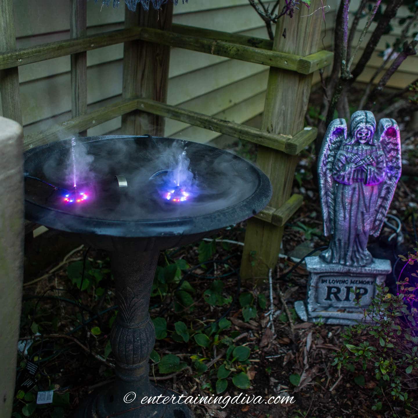 A Halloween-themed birdbath with 2 misters creating purple light and a statue of an angel.