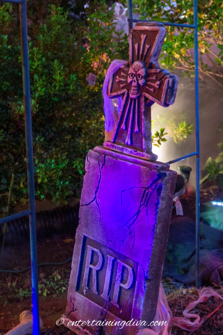 A Halloween gravestone with a cross, enhanced by blue outdoor lighting.