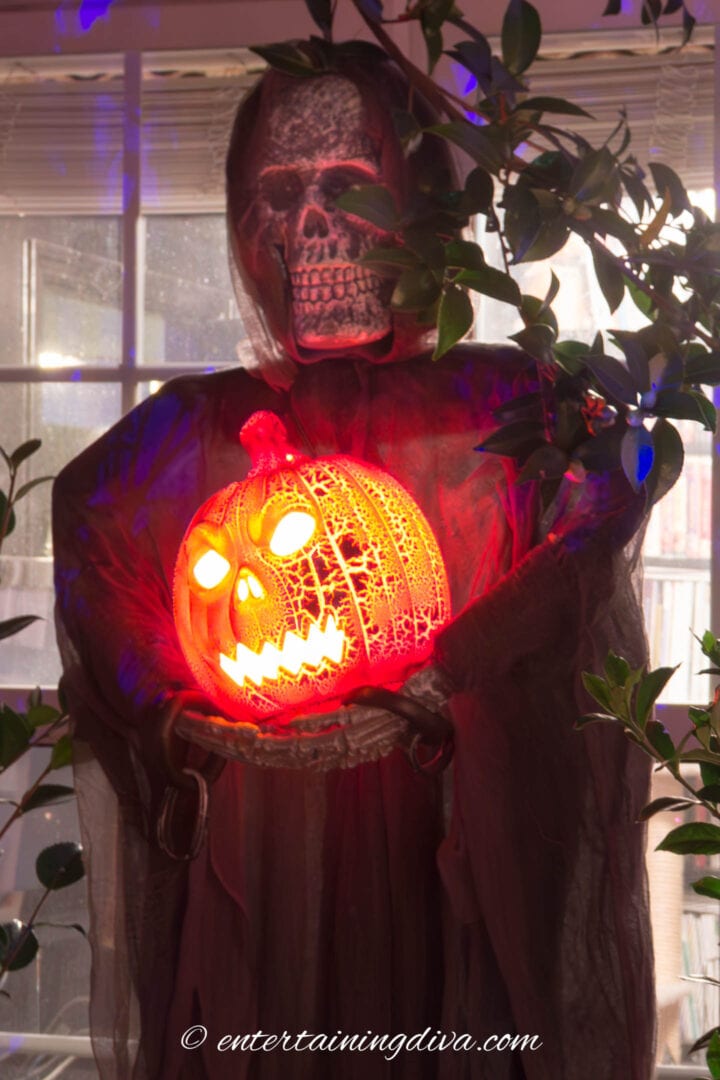A skeleton holding a pumpkin for spooky Halloween outdoor lighting.