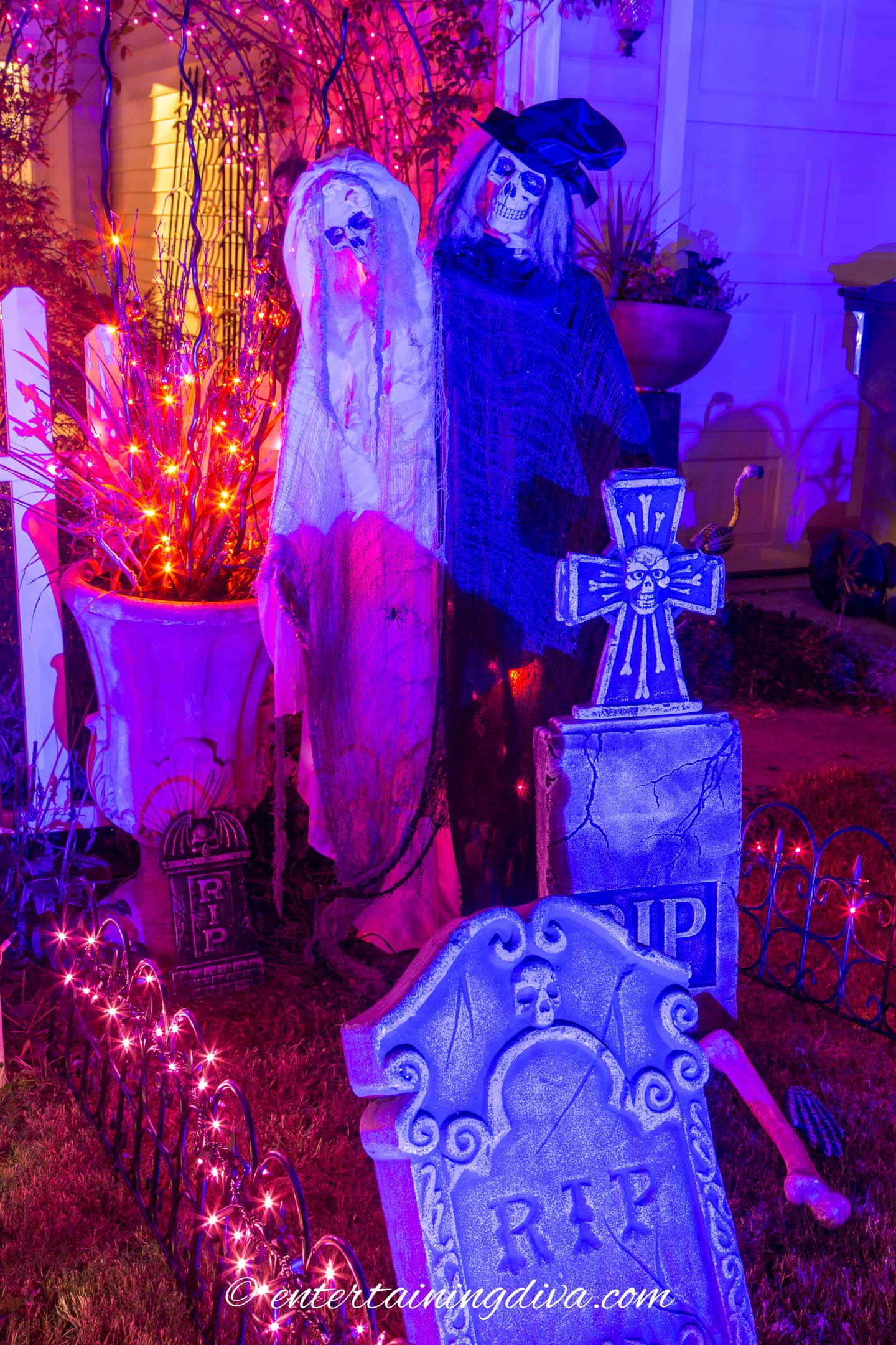Halloween ghosts and gravestones lit with a blue spotlight in a front yard.