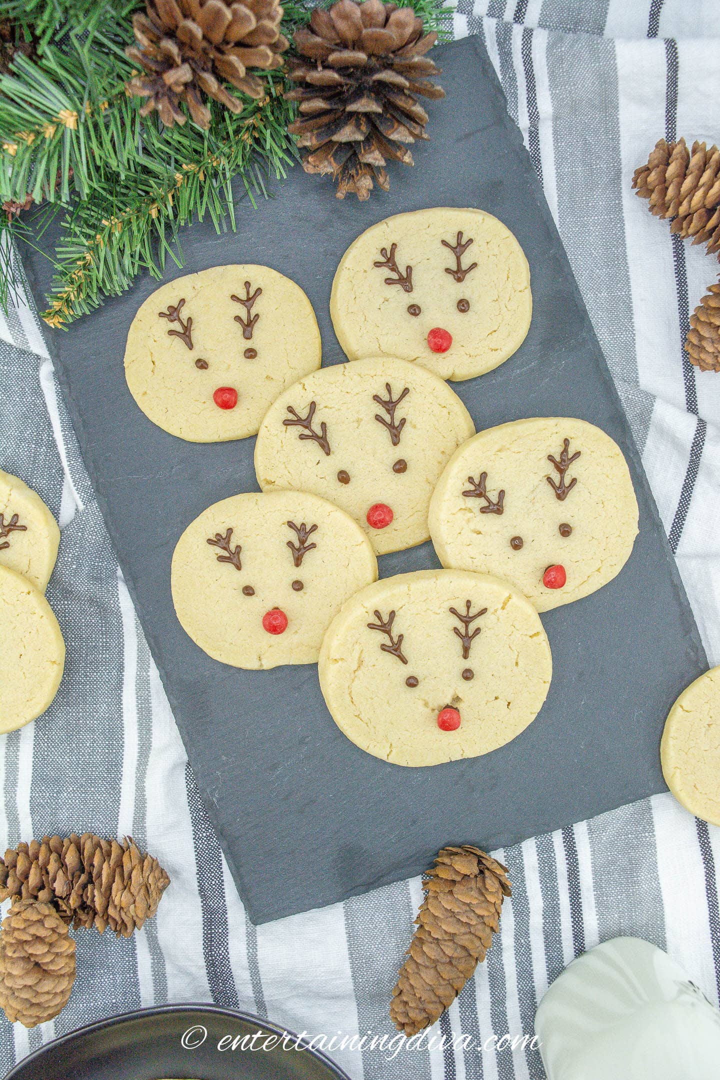 Reindeer sugar cookies and pine cones displayed on a slate serving board.