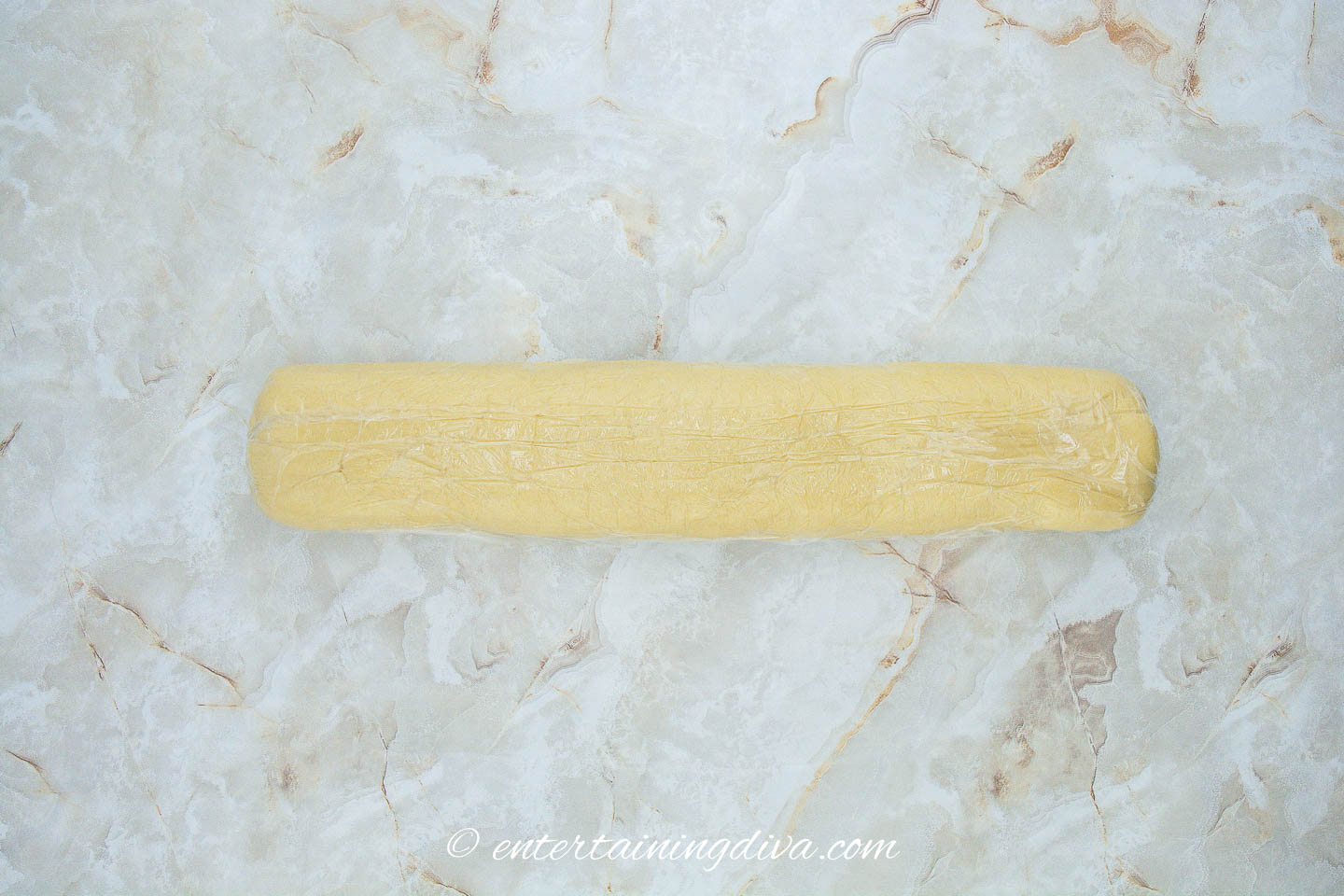A roll of cookie dough on a marble surface.