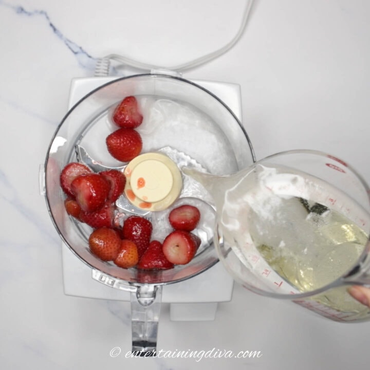 sparkling wine being poured into a food processor with strawberries in it