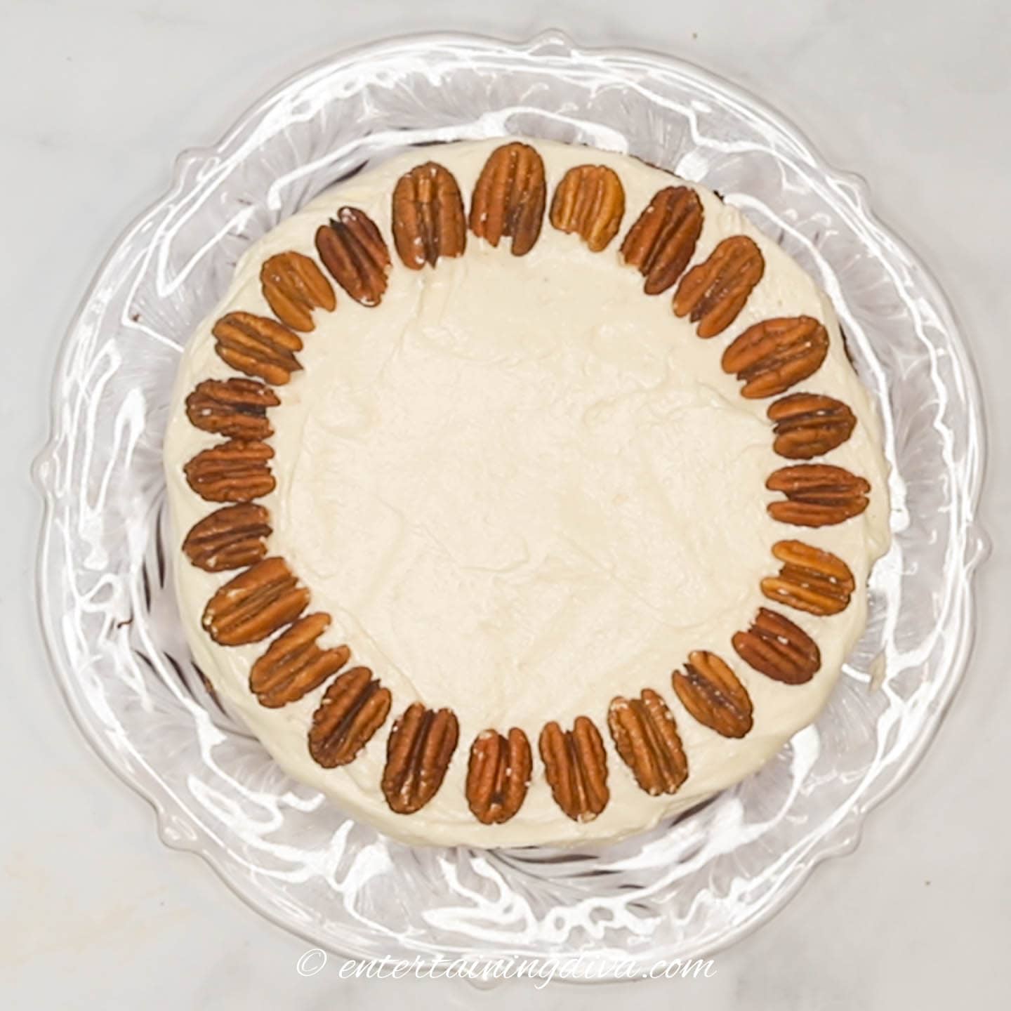 carrot cake with cream cheese icing decorated with pecans around the outside