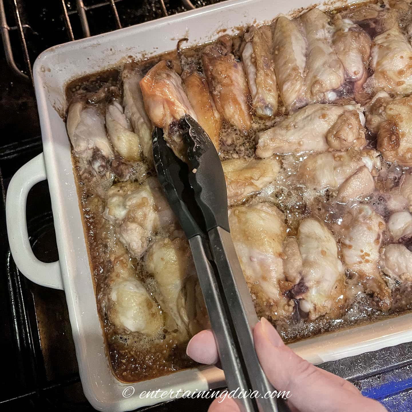 wings in a baking dish being turned over with tongs