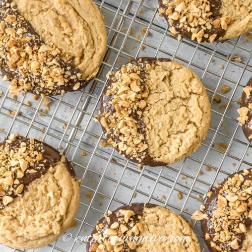 Chocolate dipped peanut butter cookies cooling with chopped peanuts as garnish on a rack.