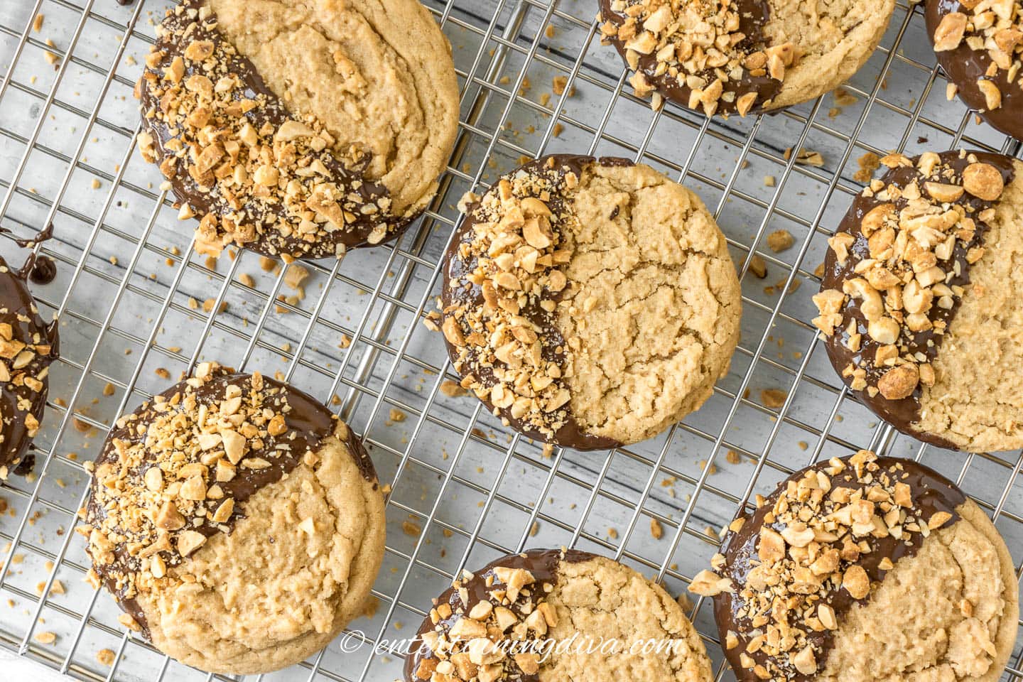 Chocolate dipped peanut butter cookies cooling with chopped peanuts as garnish on a rack.
