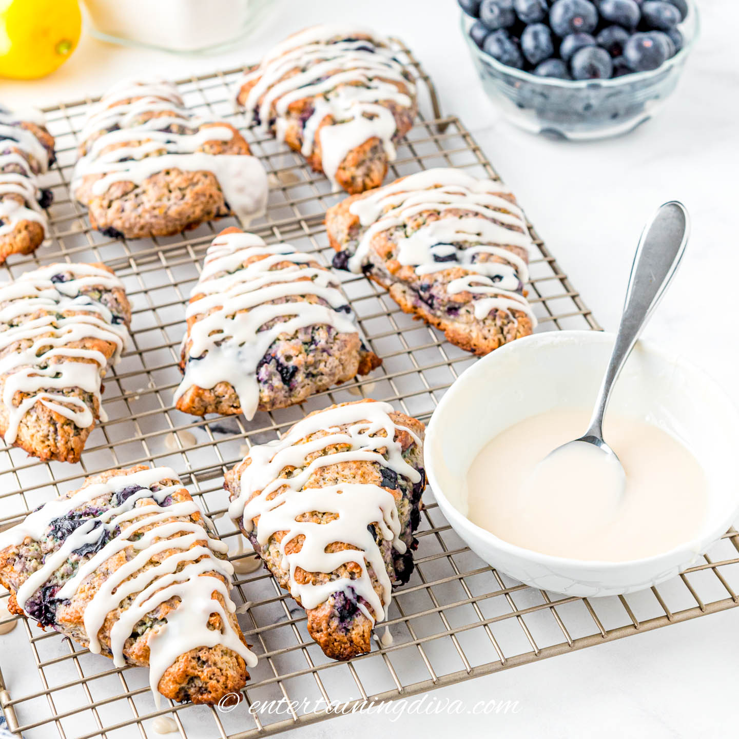 glazed lemon blueberry scones on a wire cooling rack beside a bowl of glaze
