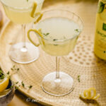 Two limoncello martinis on a tray with a bottle of lemons and a bottle of limoncello.