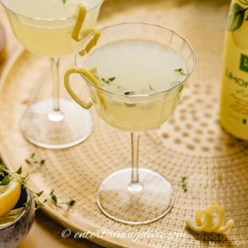 Two limoncello martinis on a tray with a bottle of lemons and a bottle of limoncello.